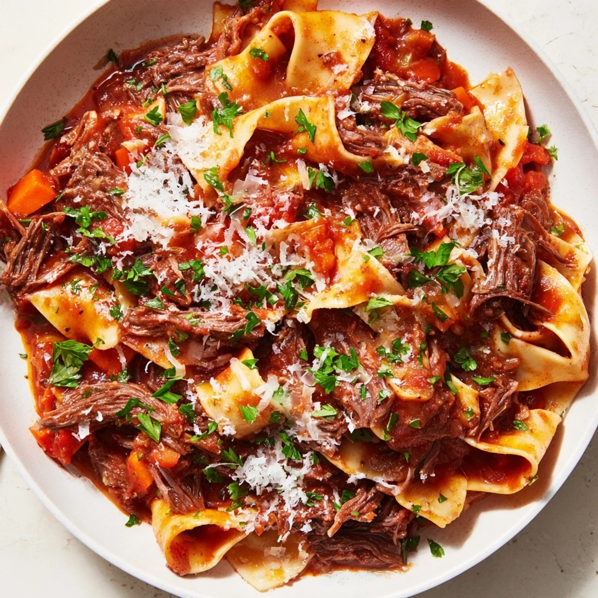 Spoonful of rich Slow Cooked Beef Ragu with pappardelle, topped with fresh herbs and Parmesan.