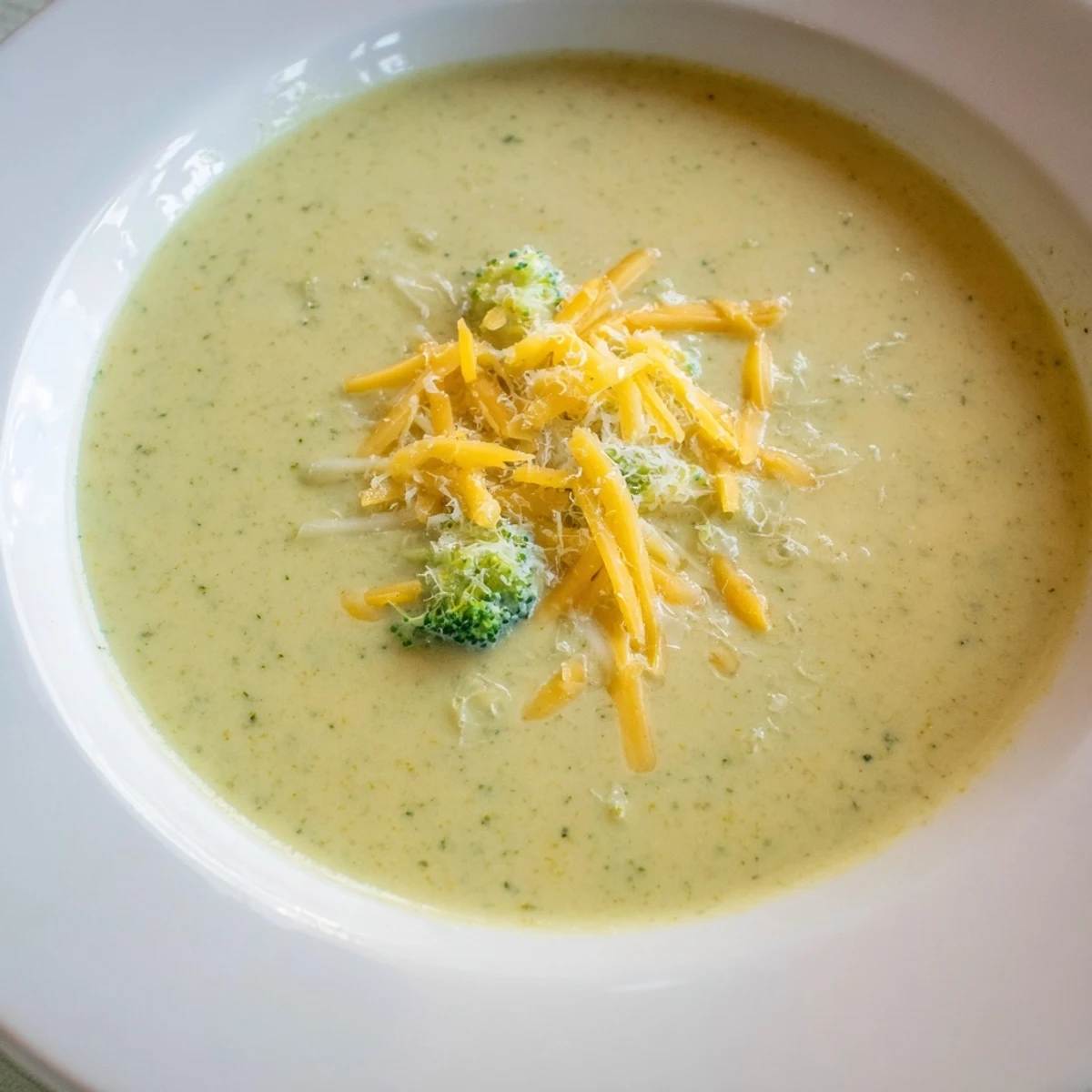 Freshly blended creamy broccoli soup with cheese, a vibrant green, ready to serve with bread.
