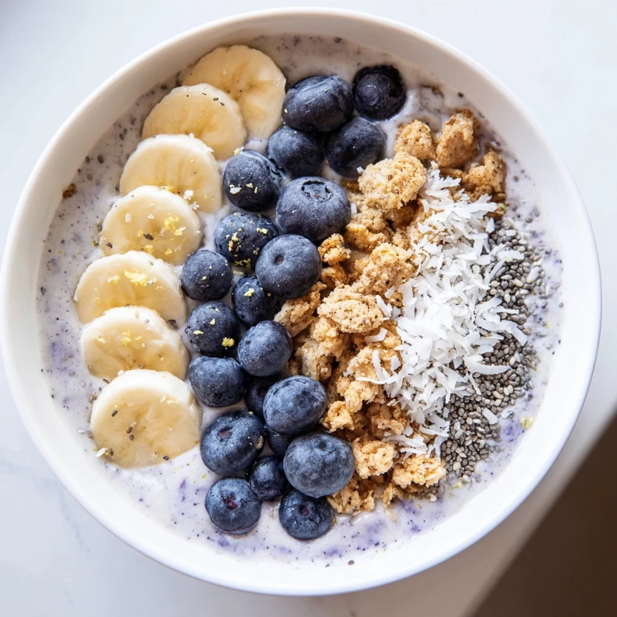 A creamy Lemon Blueberry Smoothie Bowl features a beautiful swirl of purple berries and yellow lemon zest.
