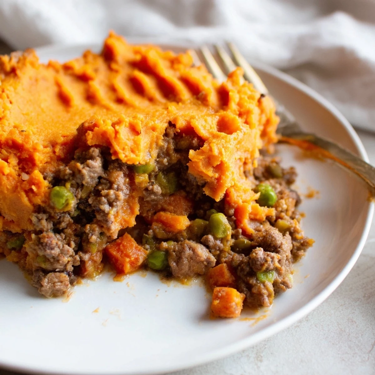 A slice of beef shepherds pie with sweet potato mash served on a white plate.
