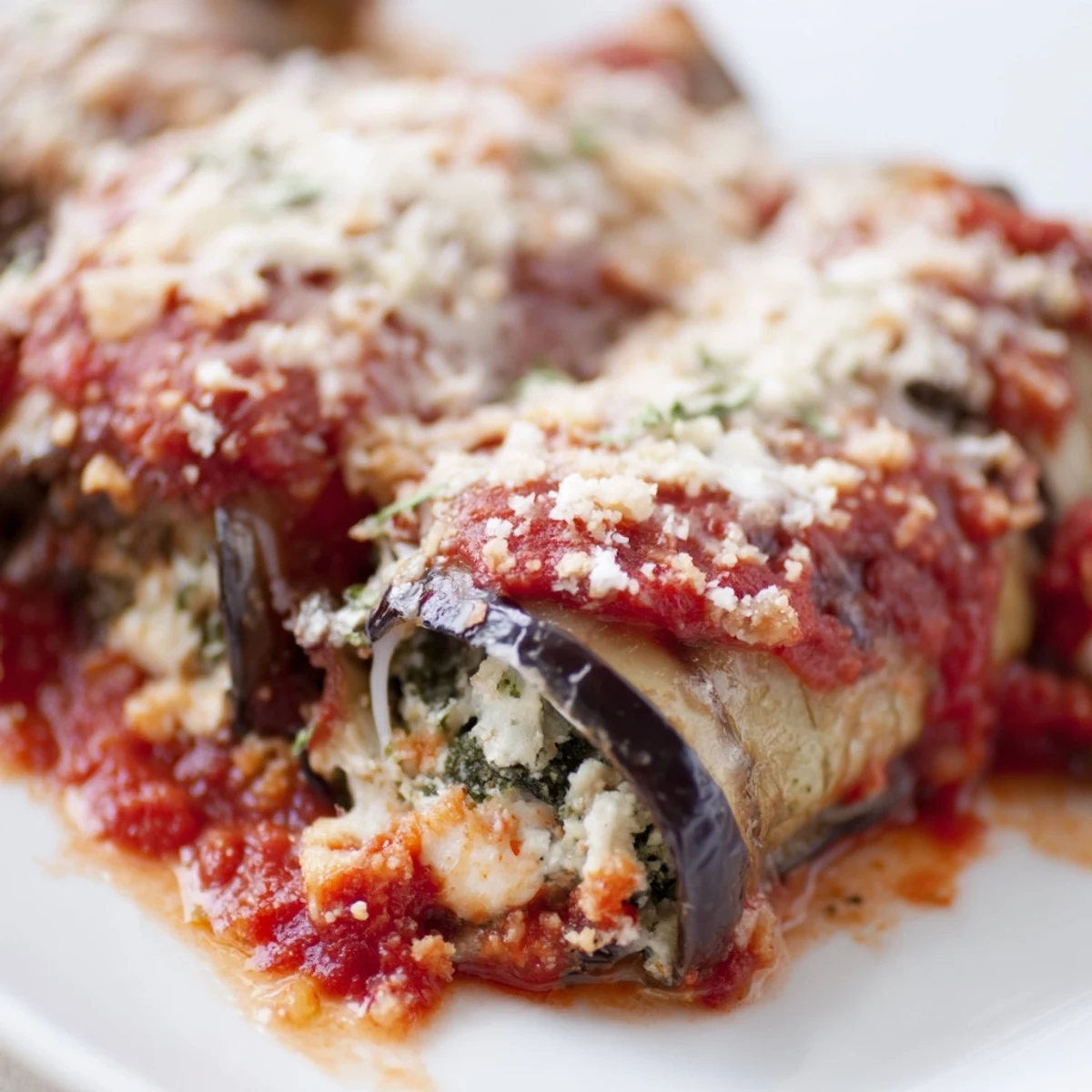 Oven-roasted eggplant slices wrapped in herby ricotta filling, arranged in a ceramic baking dish.