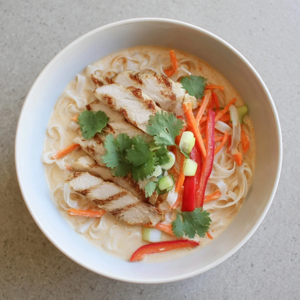 Tender grilled chicken and rice noodles in Thai Red Curry Noodle Soup with vibrant veggies.
