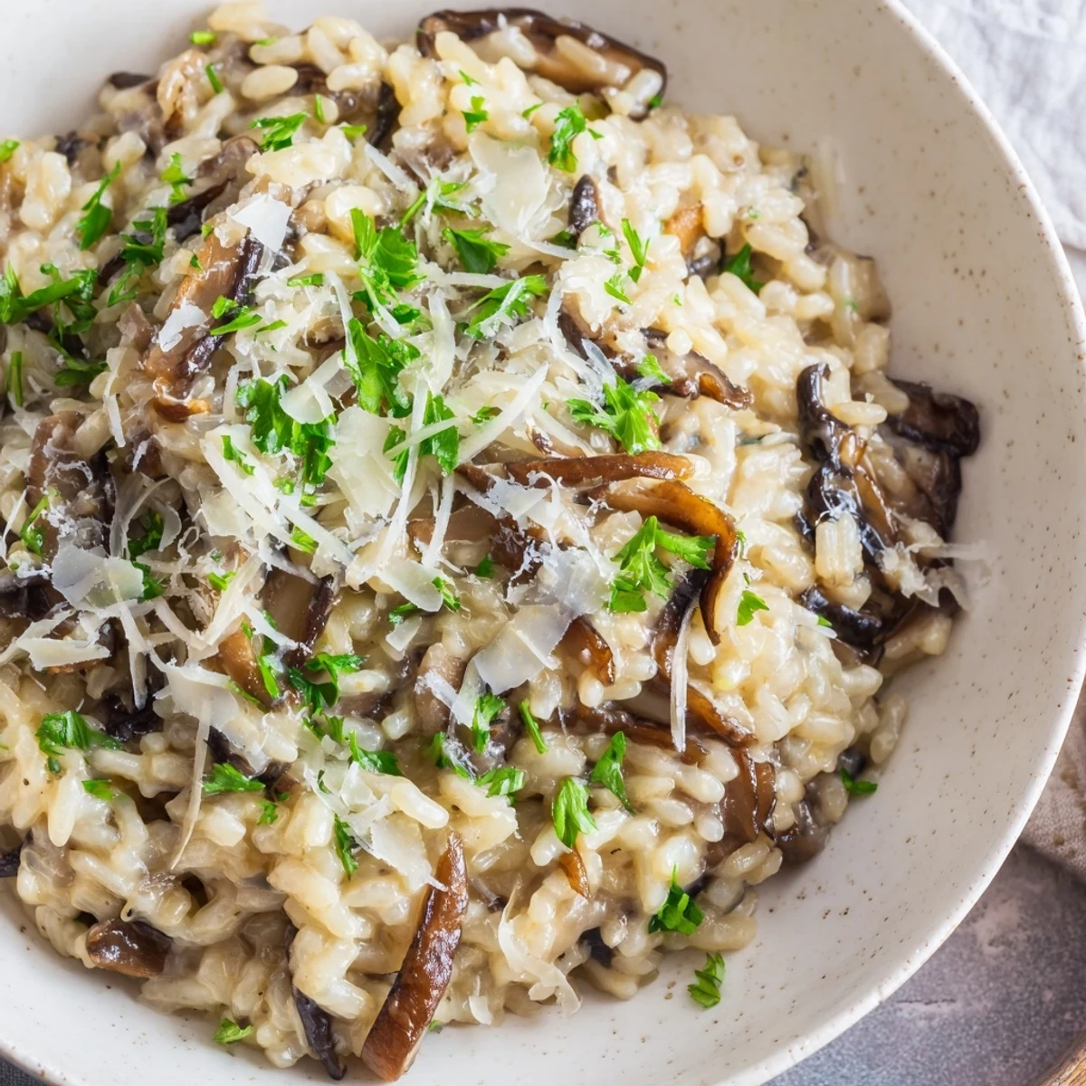 A close-up of creamy Date Night Mushroom Risotto in a shallow bowl, garnished with fresh parsley and shaved Parmesan, ready to serve.
