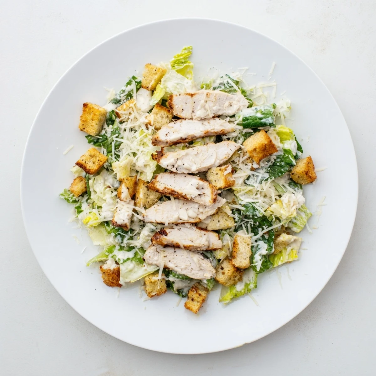 A close-up of a classic Chicken Caesar Salad, featuring juicy chicken, crisp romaine, and golden croutons tossed in a rich, creamy dressing.  