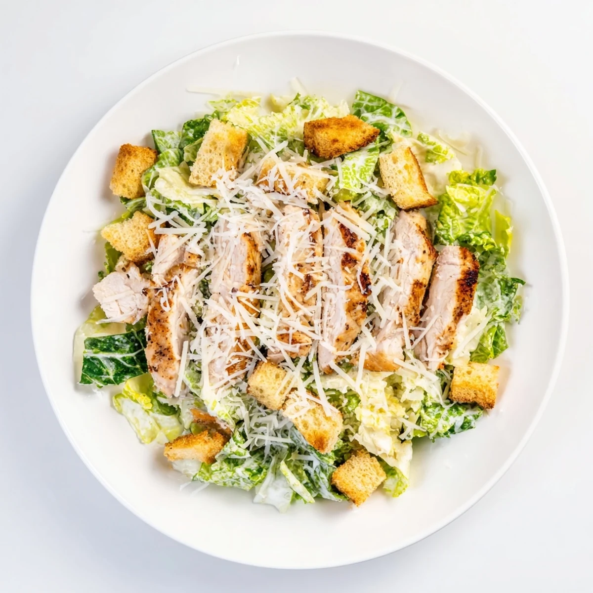 Freshly grilled chicken slices rest atop a vibrant bowl of chopped romaine, creamy Caesar dressing, and crunchy croutons, garnished with shaved Parmesan.  