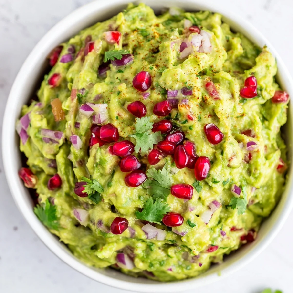 Close-up of homemade Touchdown Spicy Guacamole topped with pomegranate seeds, served with colorful veggie sticks.