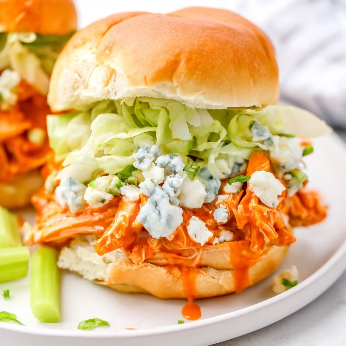 Warm buffalo chicken sliders topped with crumbled blue cheese sauce on toasted buns with fresh lettuce.