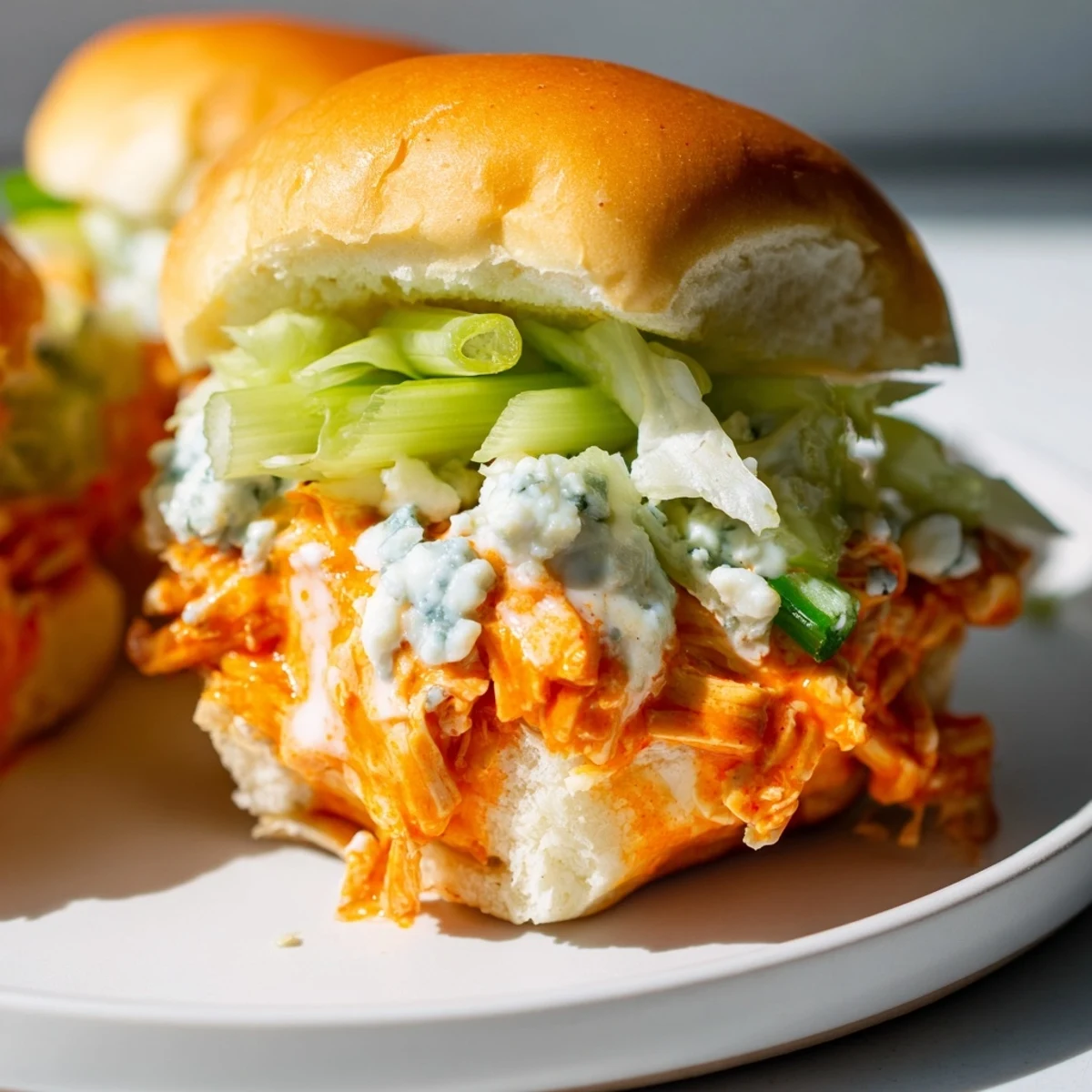 Appetizer plate of tangy buffalo chicken sliders with blue cheese drizzle, chives, and fresh lettuce.