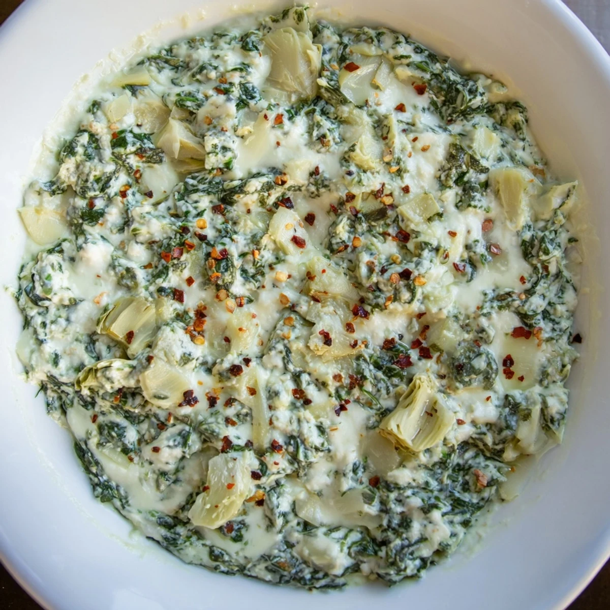 Golden bubbly Spinach Dip with Artichokes and Cheese, baked in a white dish, served with crunchy crostini for dipping.