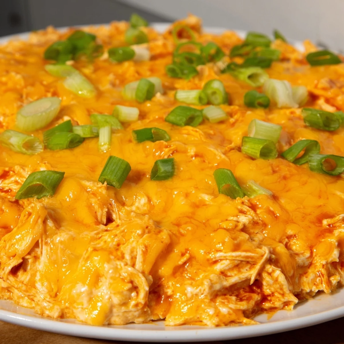 Creamy Spicy Buffalo Chicken Dip with Tortilla Chips bubbly in a dish, topped with melted cheese.