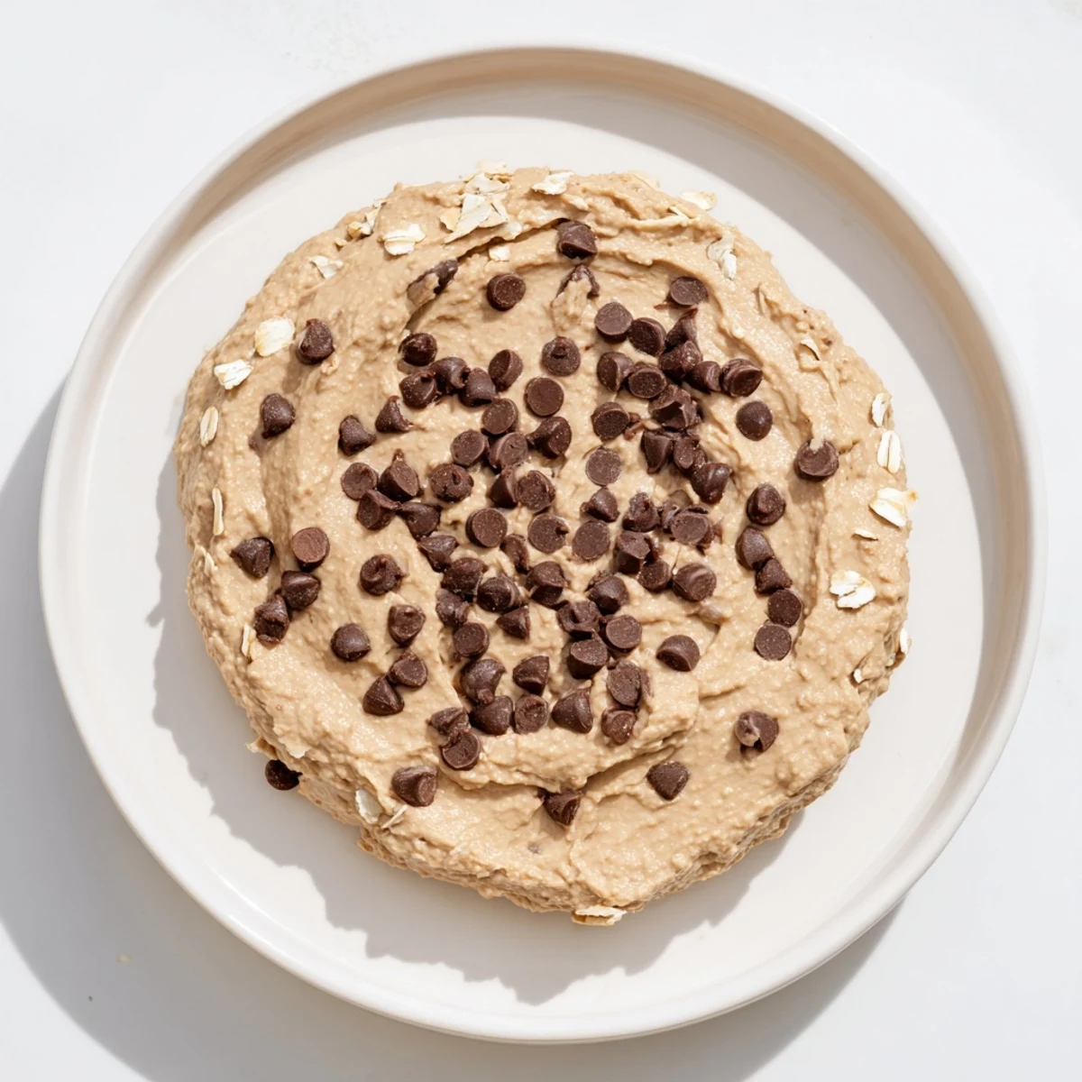 A small jar of chocolate chip cookie dough hummus topped with mini chocolate chips and a drizzle of maple syrup.