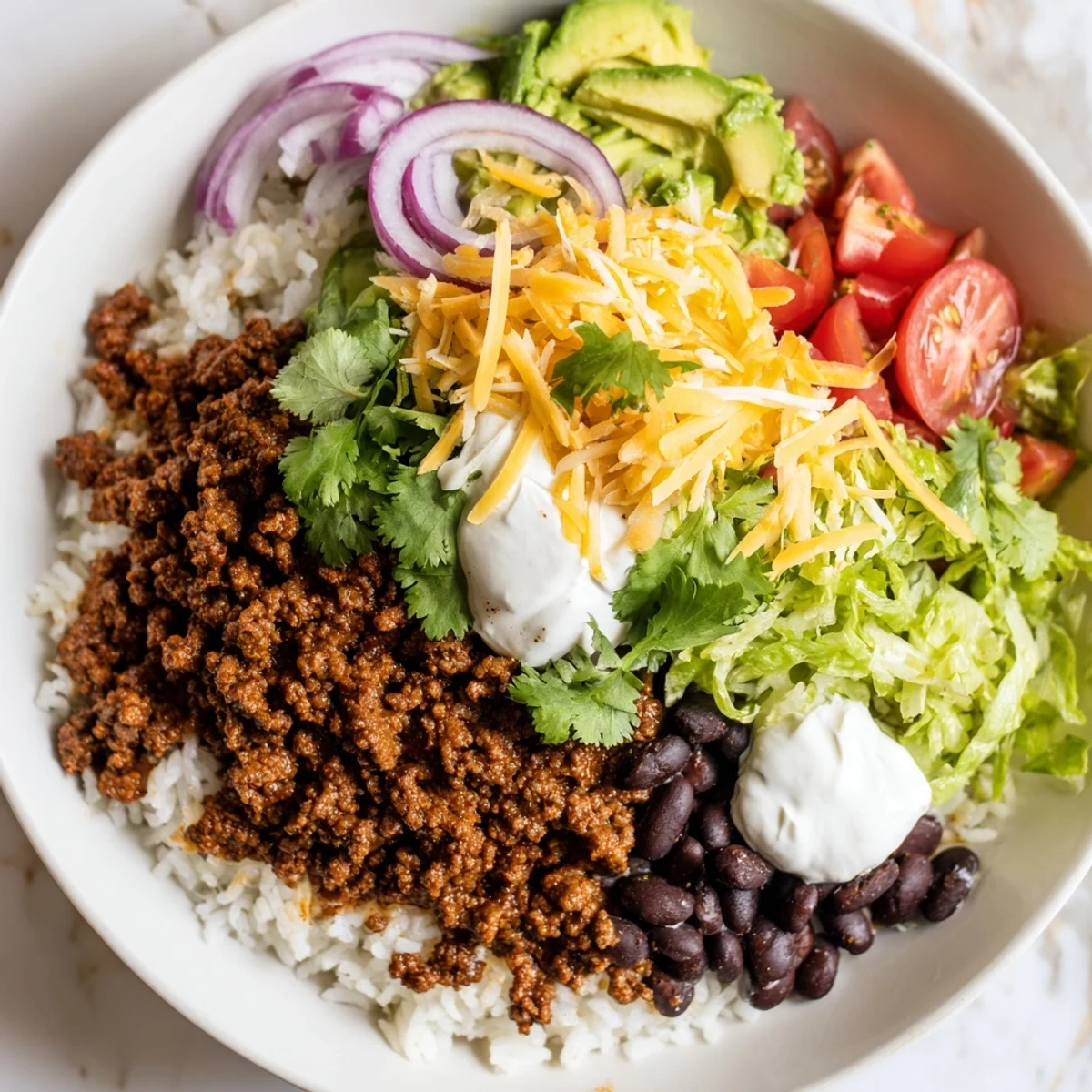 Close-up view of savory beef burrito bowls featuring tender seasoned beef, warm black beans, and fluffy rice, garnished with shredded cheese, sour cream, and fresh cilantro leaves.
