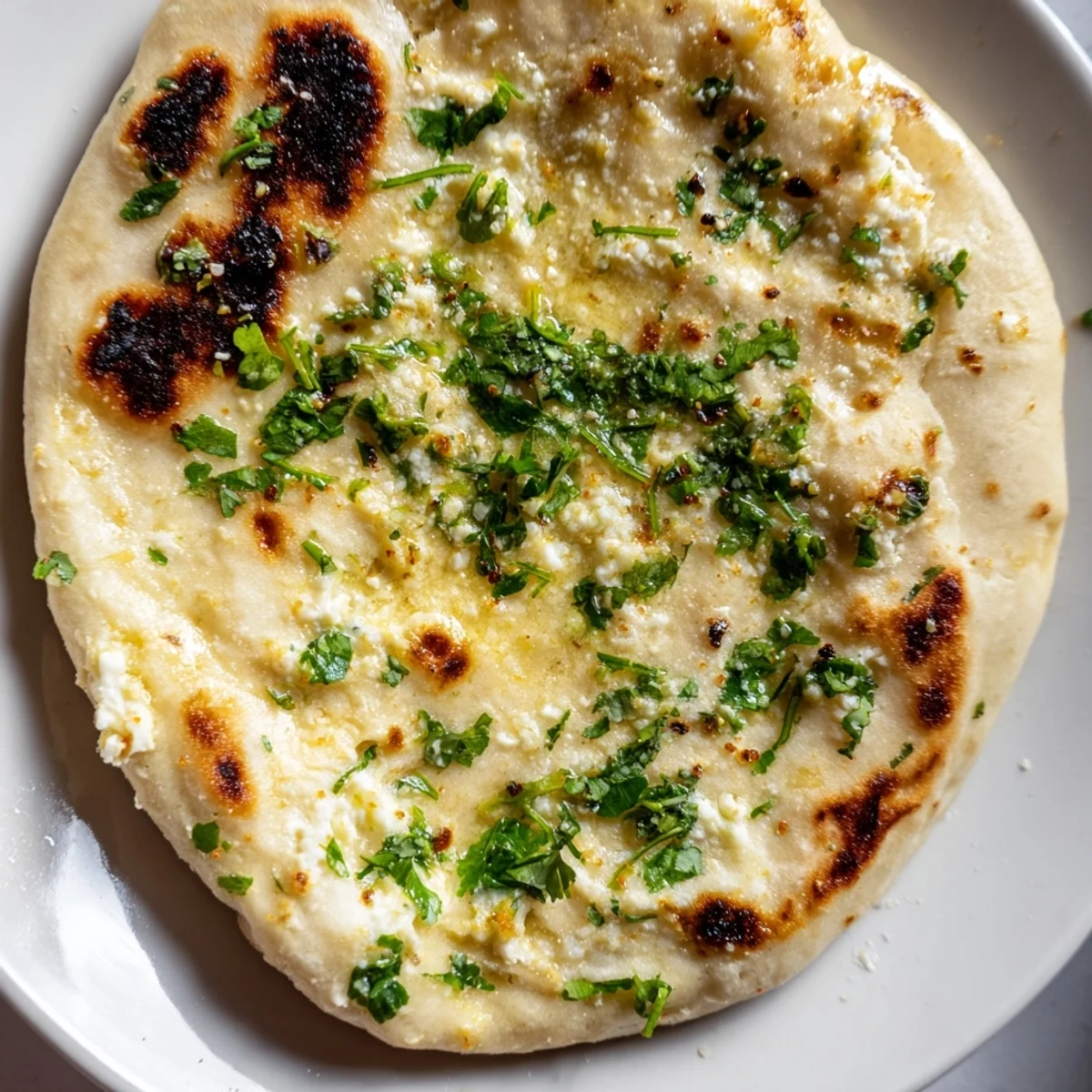 A close-up of stuffed Cottage Cheese Garlic Naan revealing creamy filling, golden charred spots, and garlic butter brushed on top.