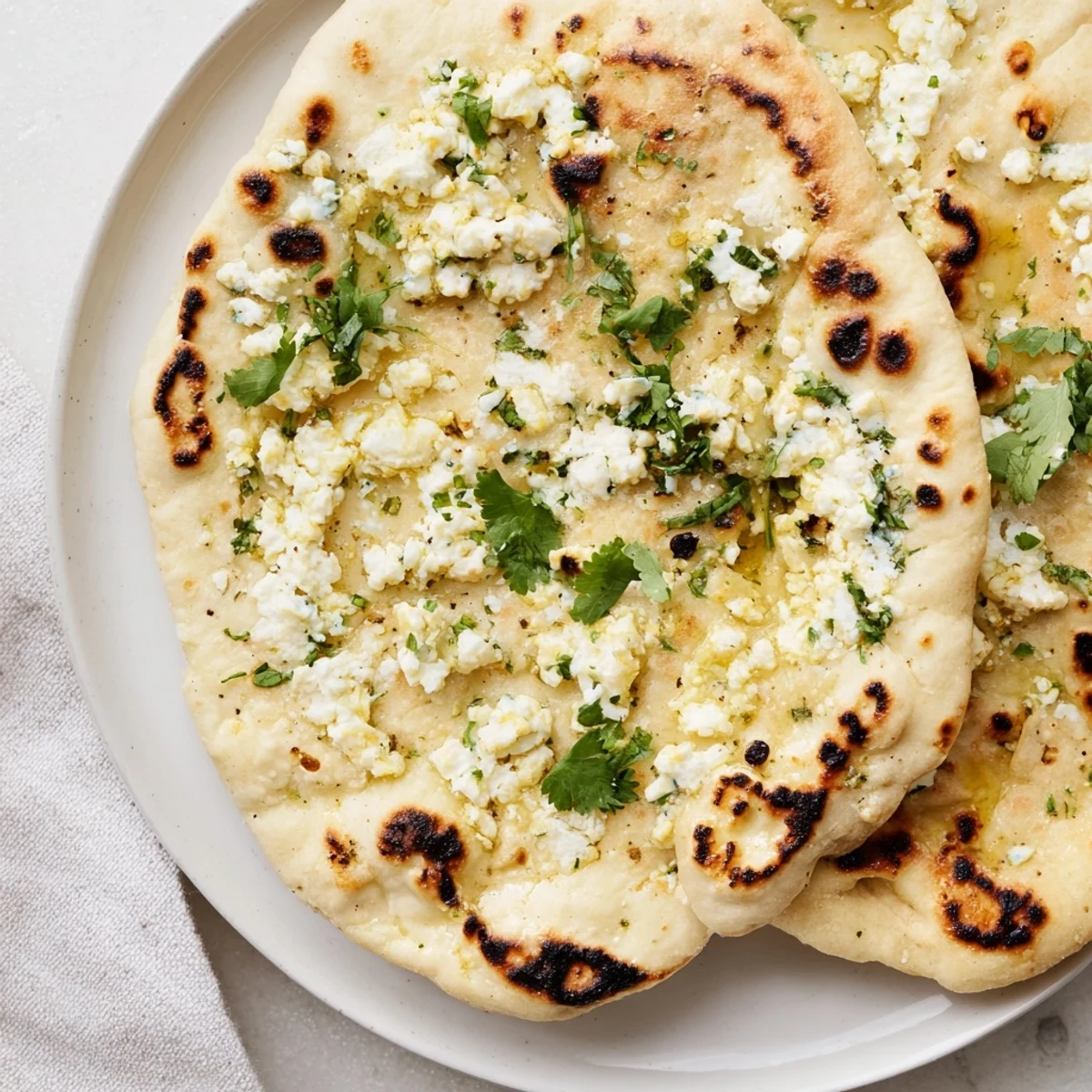 Freshly cooked Cottage Cheese Garlic Naan with melted butter and cilantro, served warm alongside a bowl of curry.