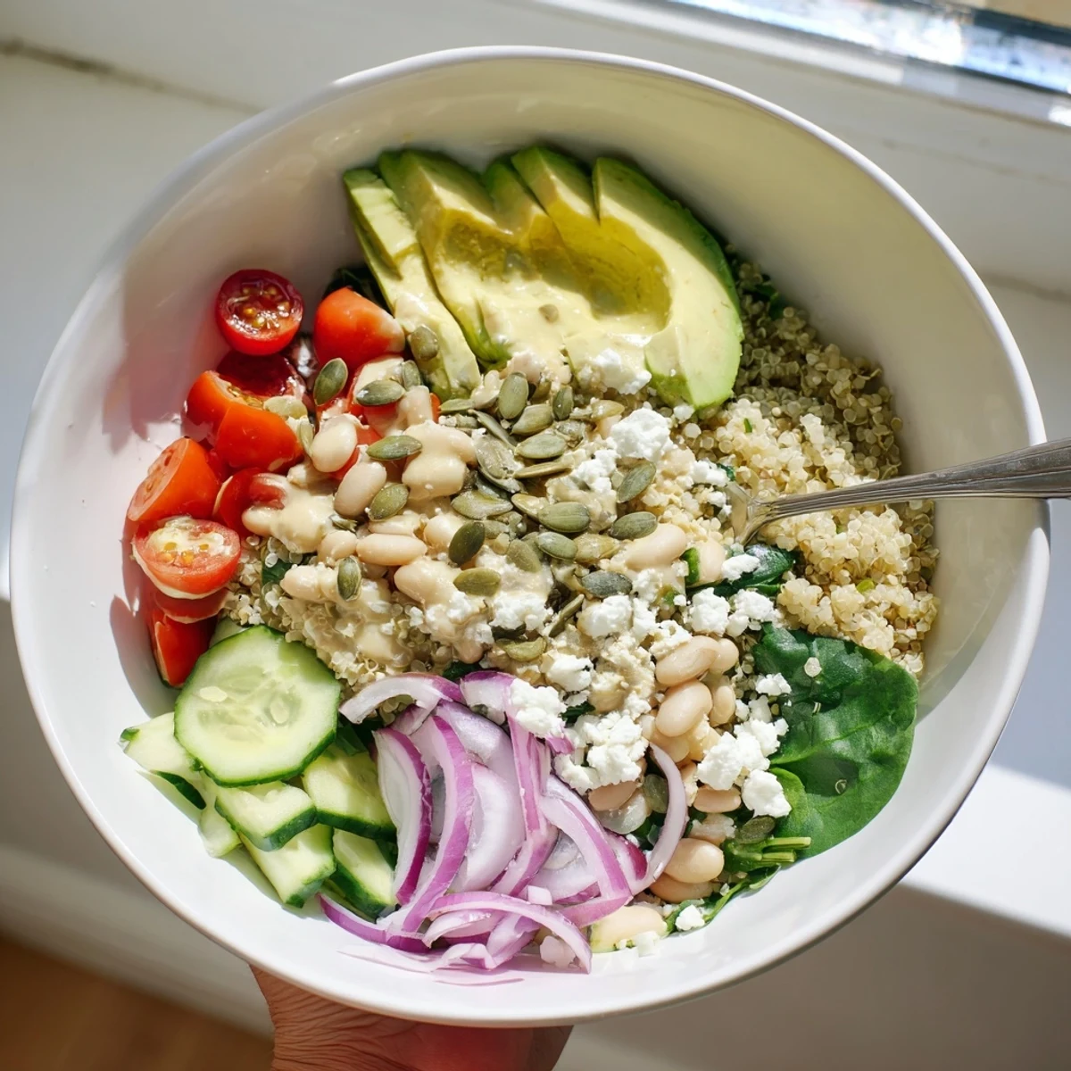 A vibrant Spinach & White Bean Ultimate Protein Power Bowl topped with sliced avocado, pumpkin seeds, and creamy lemon-tahini dressing.