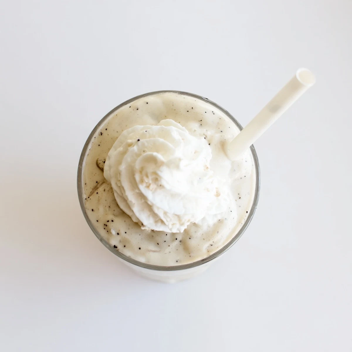 Creamy Vanilla Bean Frappuccino topped with whipped cream in a tall glass on a marble counter.