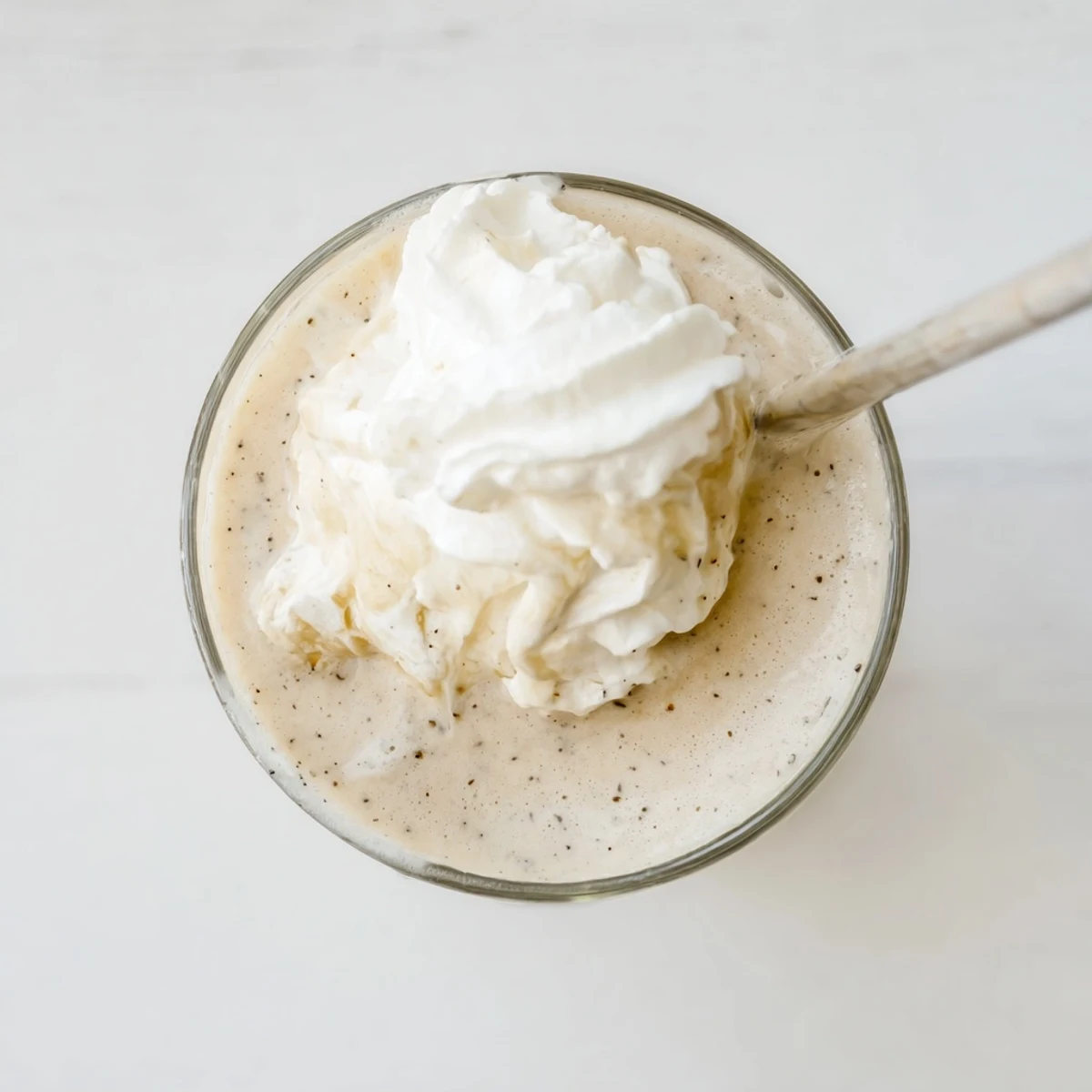 A frosted glass of Vanilla Bean Frappuccino shows real vanilla specks and melting ice cream.