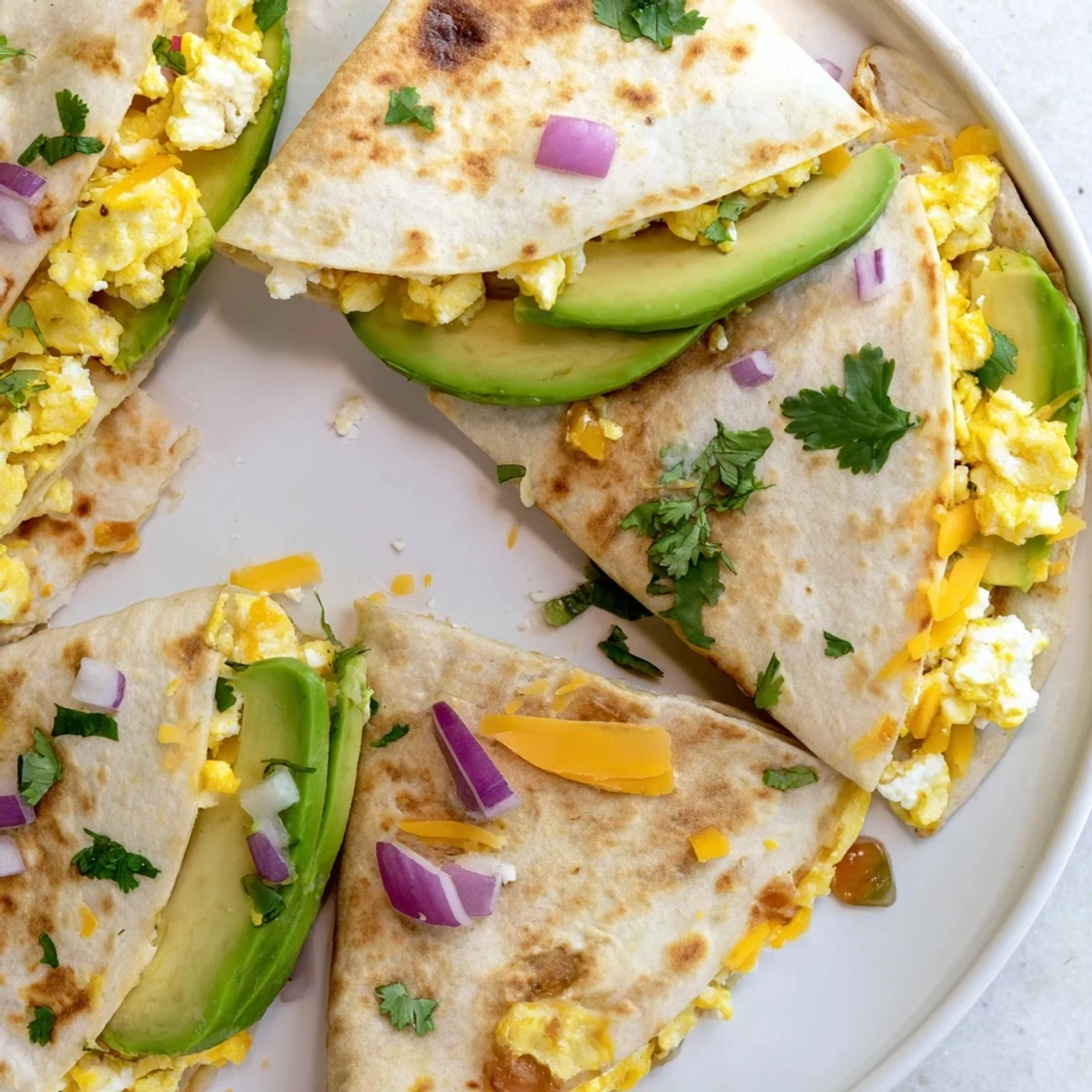 Golden-brown Spicy Avocado Egg and Three Cheese Quesadillas are cut into wedges on a plate, revealing melted cheddar and Monterey Jack.