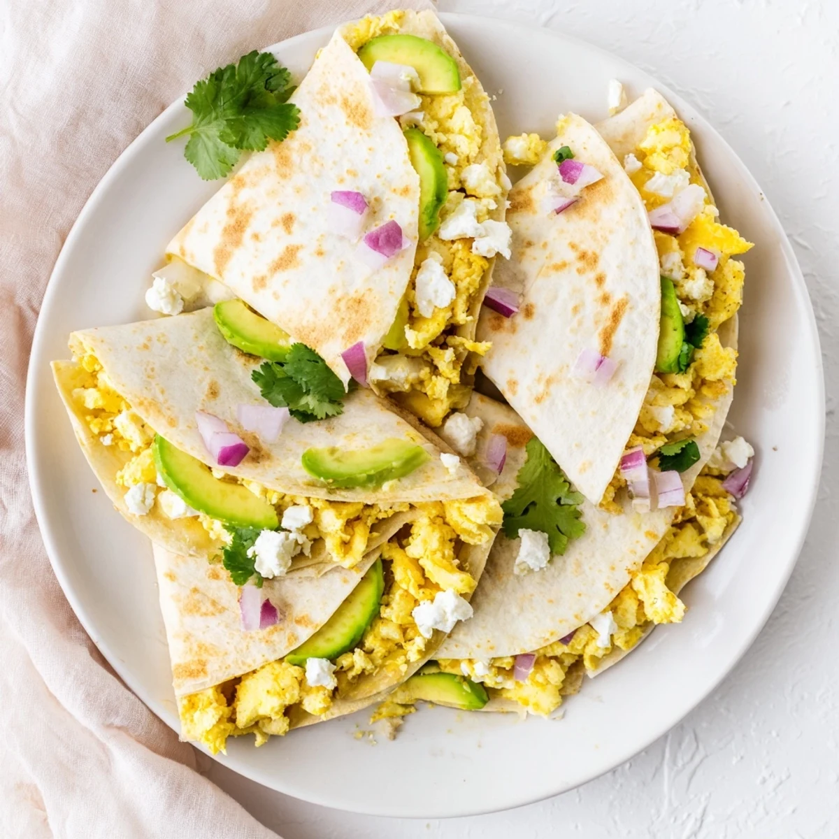 A close view of Spicy Avocado Egg and Three Cheese Quesadillas filled with creamy avocado slices, fluffy scrambled eggs, and crumbled feta.