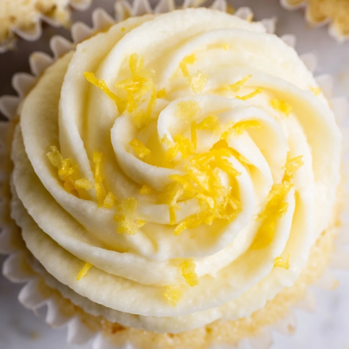 A plate of four freshly baked Limoncello Cupcakes with golden-yellow crumb and fluffy lemon buttercream swirls, garnished with fresh lemon zest.