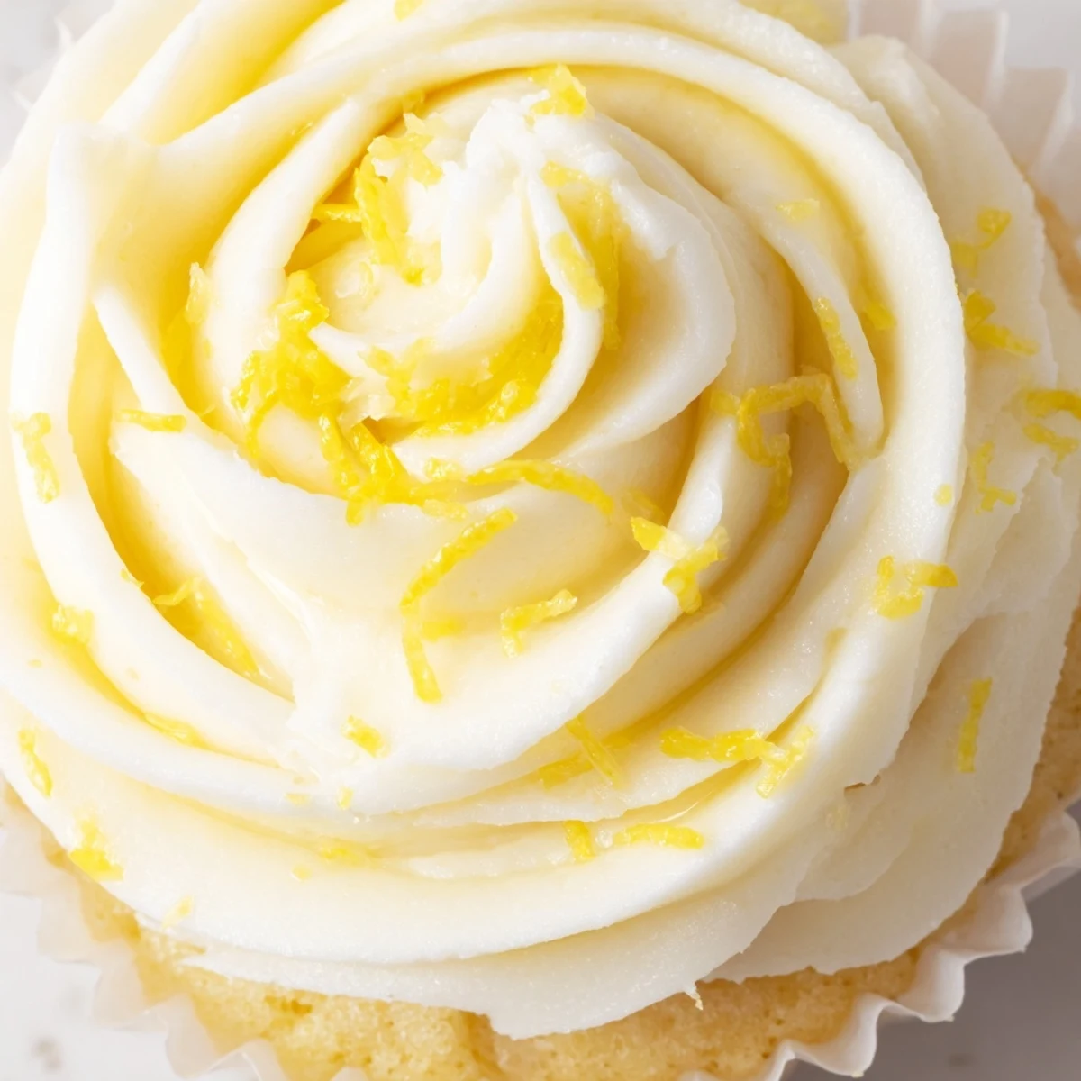 A close-up of a Limoncello Cupcake on a marble counter, showing moist cake and tangy lemon limoncello buttercream frosting with a lemon twist garnish.