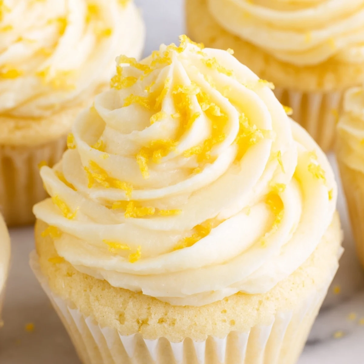 Overhead view of twelve Limoncello Cupcakes arranged on a white platter for summer entertaining, with bright yellow frosting and zesty citrus aroma.