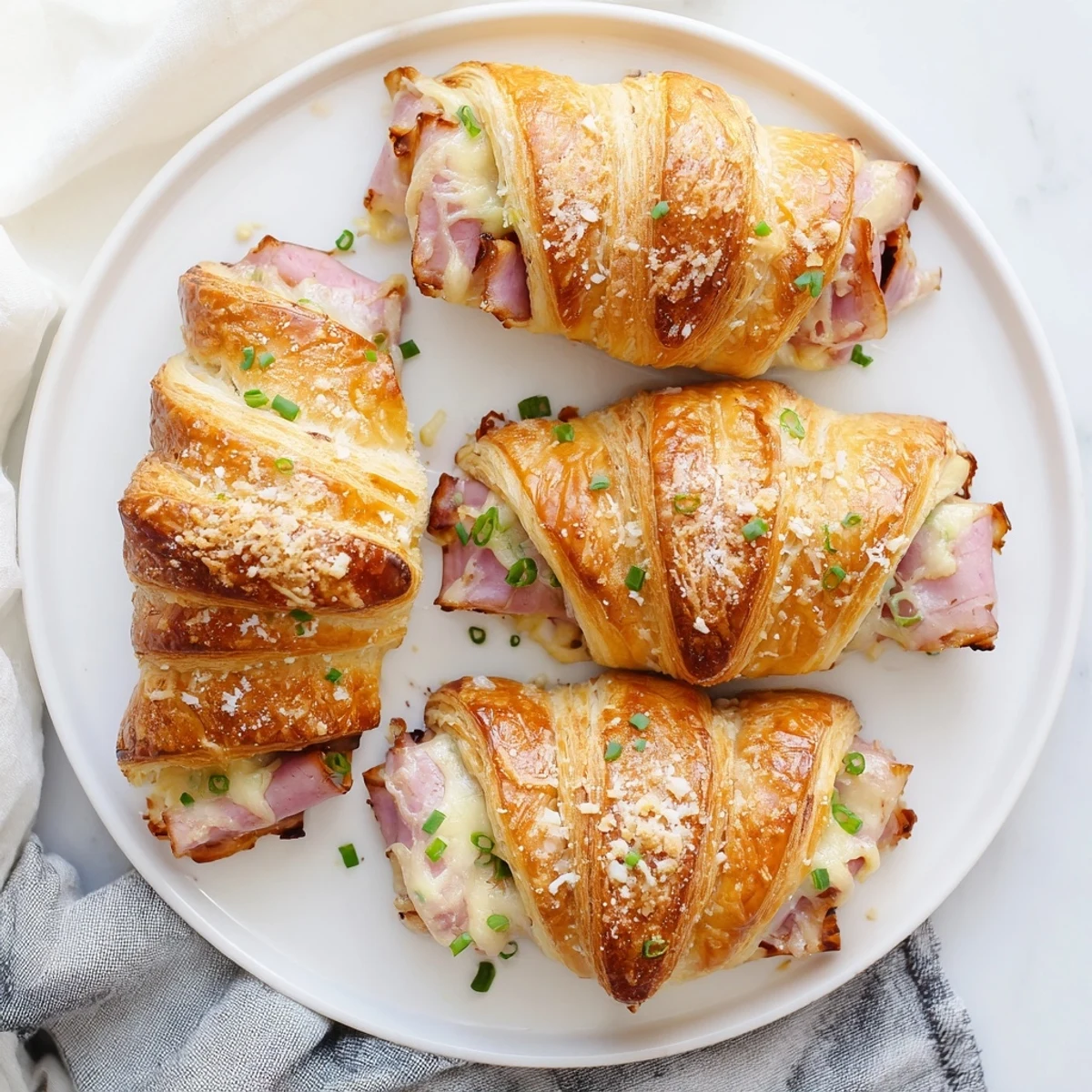Flaky Stuffed Croissants rest on a rustic plate, stuffed with savory ham and cheese and topped with chives.