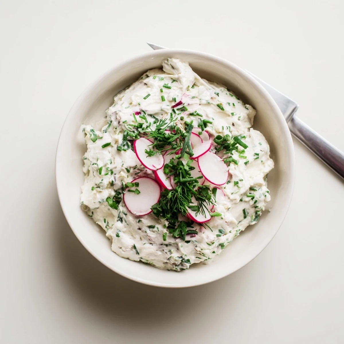Freshly made Simple Easter Herb Cheese Dip in a white bowl, garnished with chopped chives and dill, ready for serving.