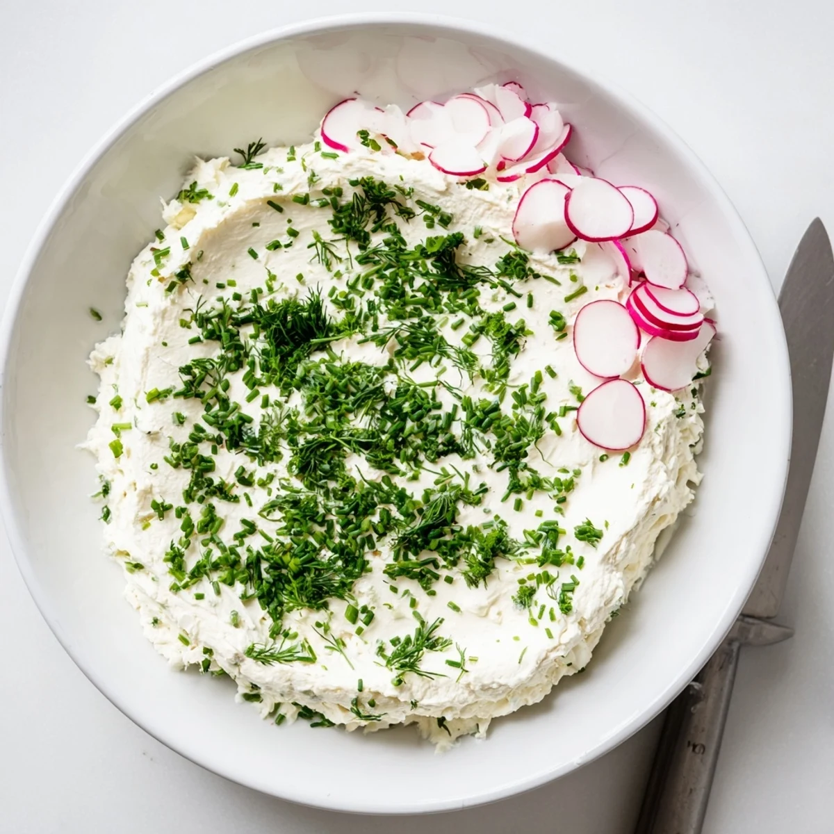 Smooth and creamy Simple Easter Herb Cheese Dip topped with radish slices and edible flowers in a festive serving dish.