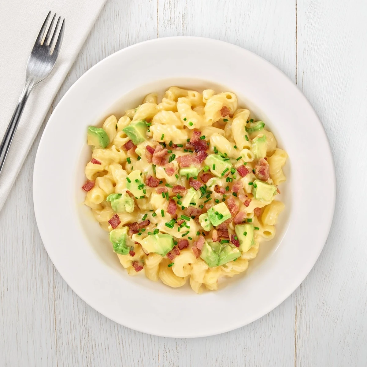 A close up of rich avocado and bacon mac and cheese with crispy bacon bits on top.