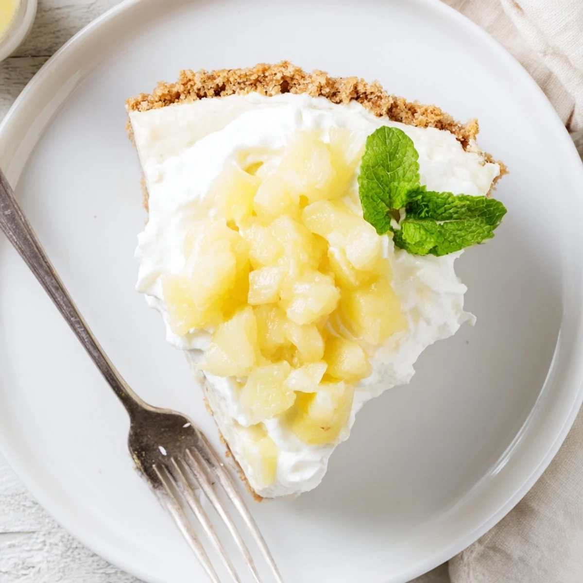 No Bake Pineapple Cheesecake topped with whipped cream and mint, showing creamy texture on graham crust.