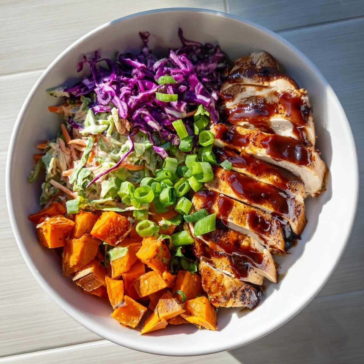Golden roasted sweet potatoes topped with glazed BBQ chicken slices and crunchy purple cabbage coleslaw in a meal prep bowl