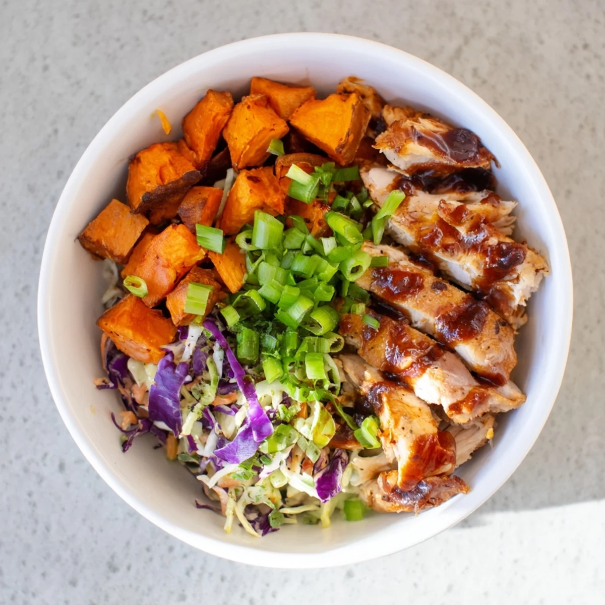 Hearty BBQ chicken bowl featuring tender sliced chicken breast over caramelized sweet potato cubes with fresh creamy coleslaw