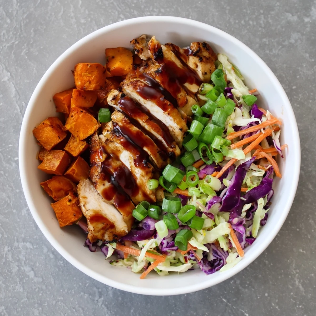 Vibrant grain-free bowl stacked with smoked BBQ chicken, roasted sweet potatoes, and tangy coleslaw garnished with green onions