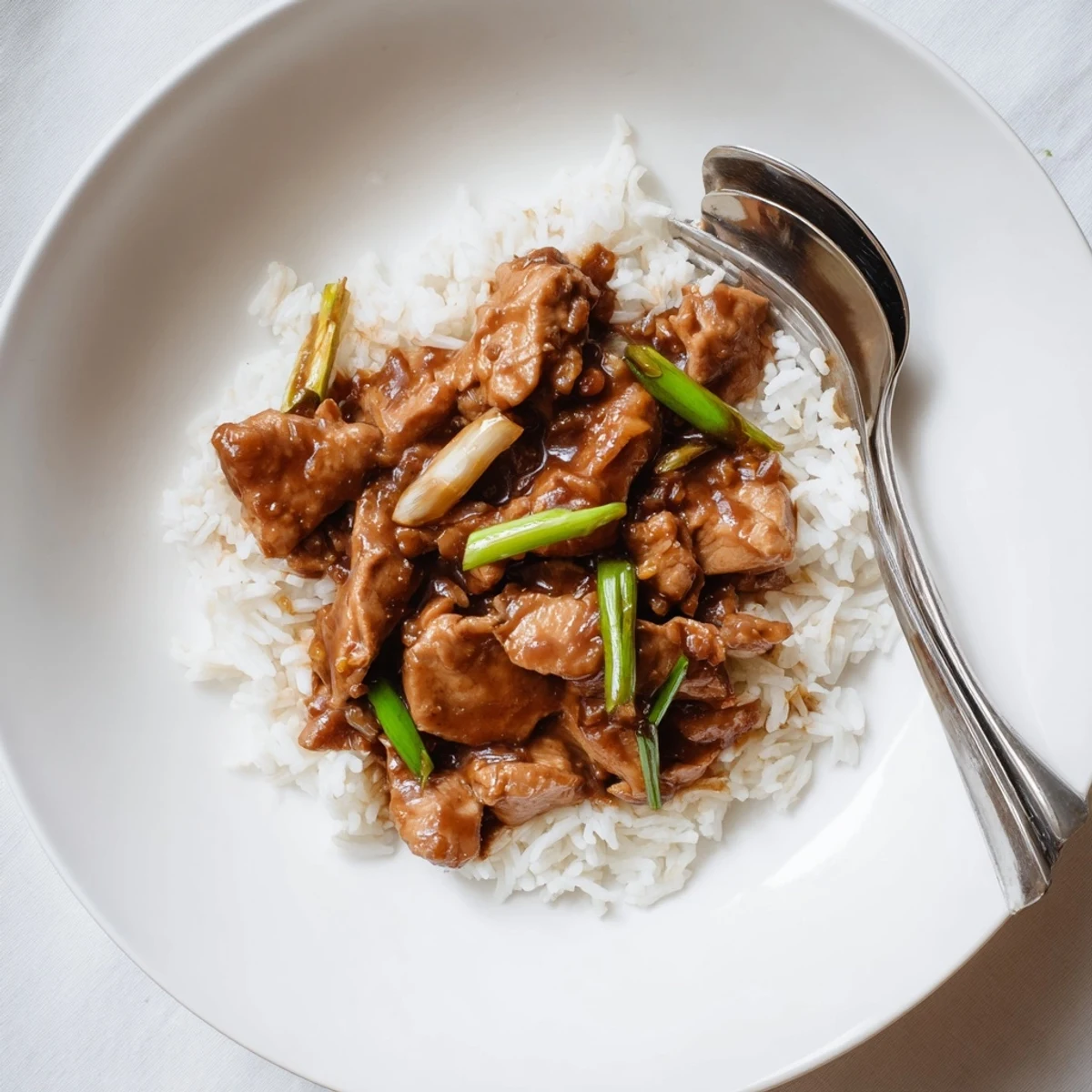 Homemade Mongolian chicken in thick caramelized sauce served over fluffy rice with sesame seed garnish