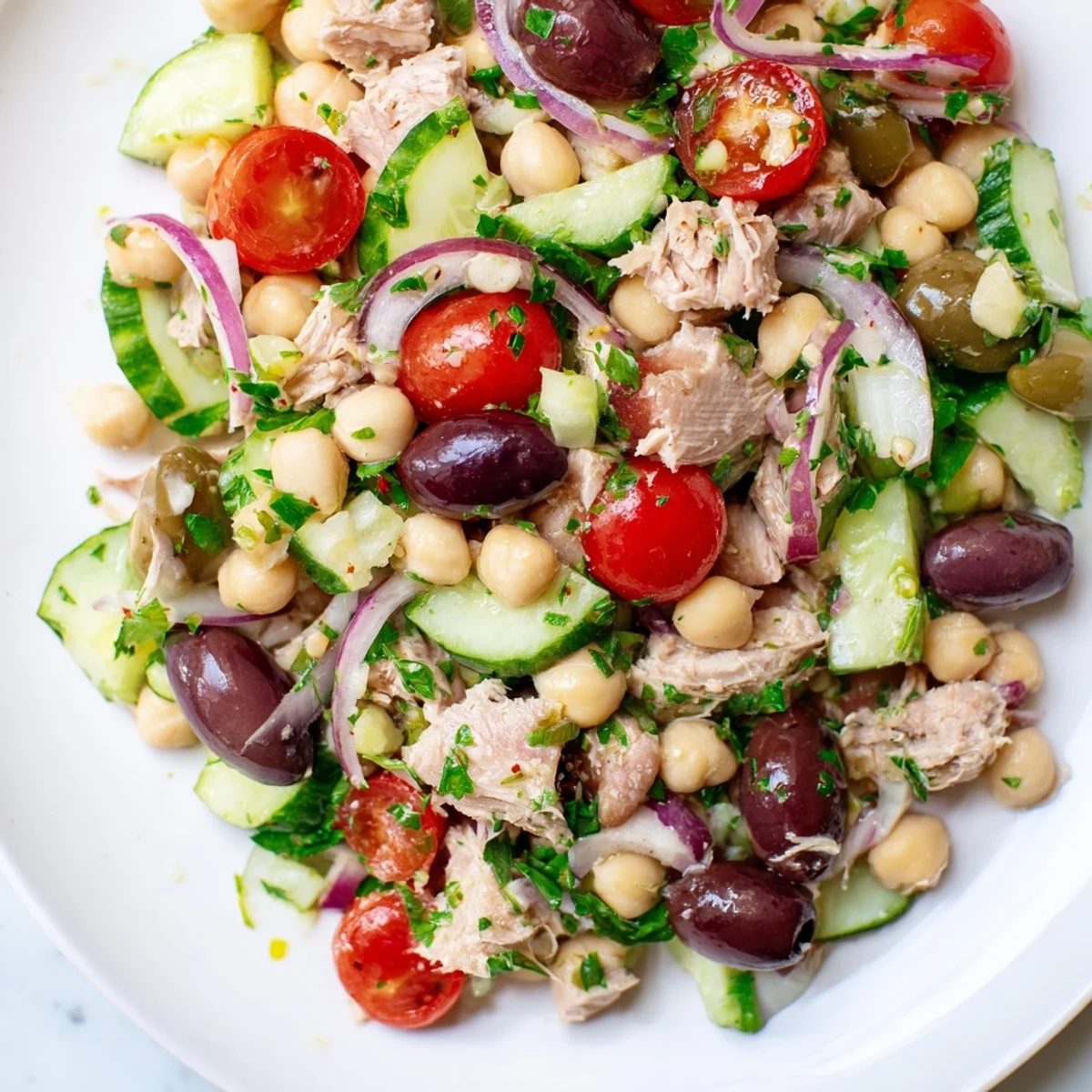 Mediterranean-inspired hearty tuna and garbanzo bean salad plated with crisp vegetables, briny olives, and chopped fresh parsley