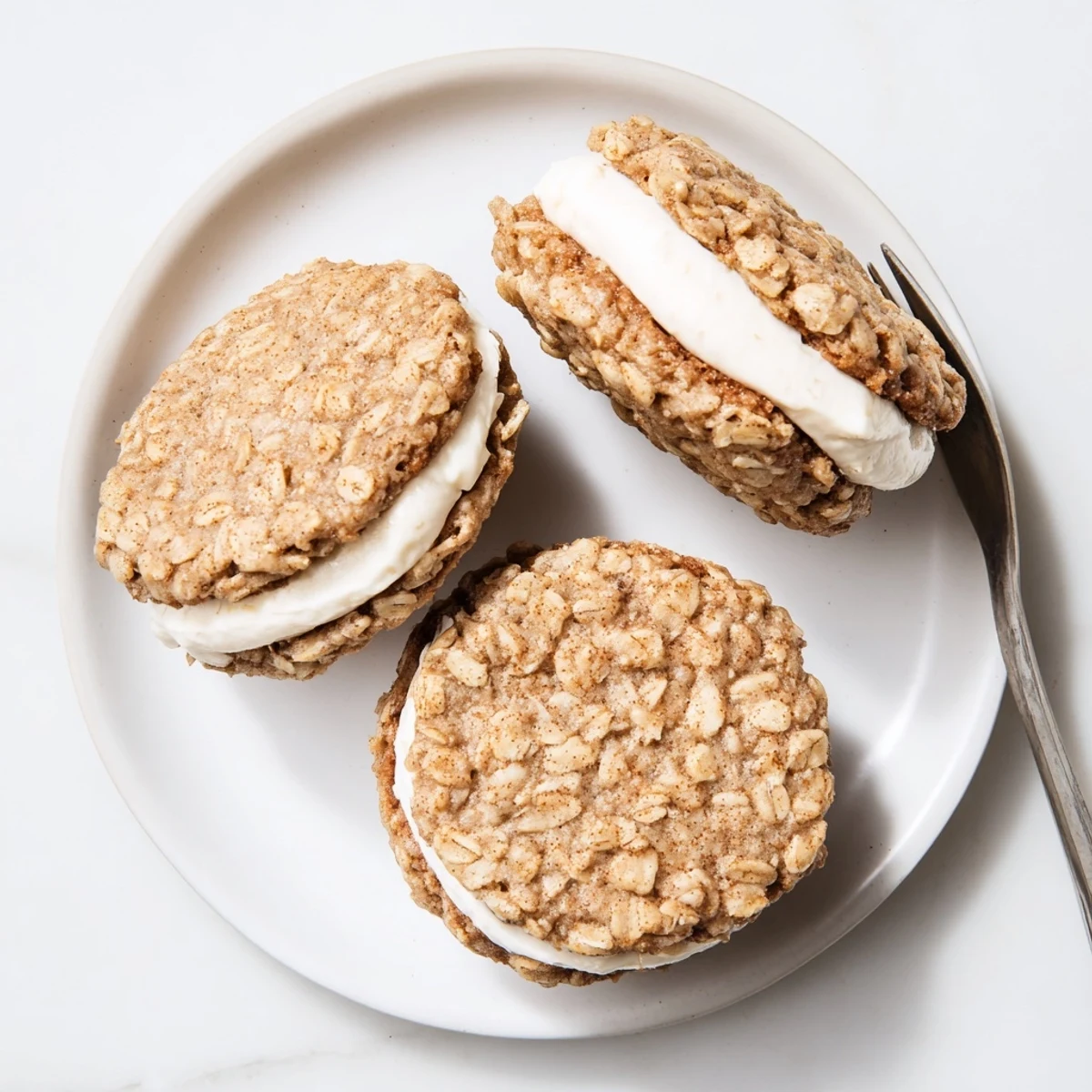 Close-up view of a homemade oatmeal cream pie sandwich displaying the thick creamy vanilla filling pressed between golden brown oatmeal cookies