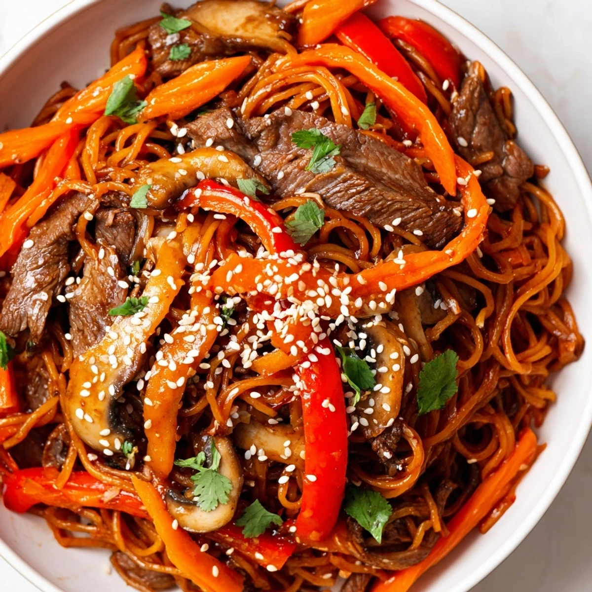 Plate of Korean beef noodles featuring marinated beef, julienned carrots, bell peppers, and mushrooms tossed in spicy sesame dressing