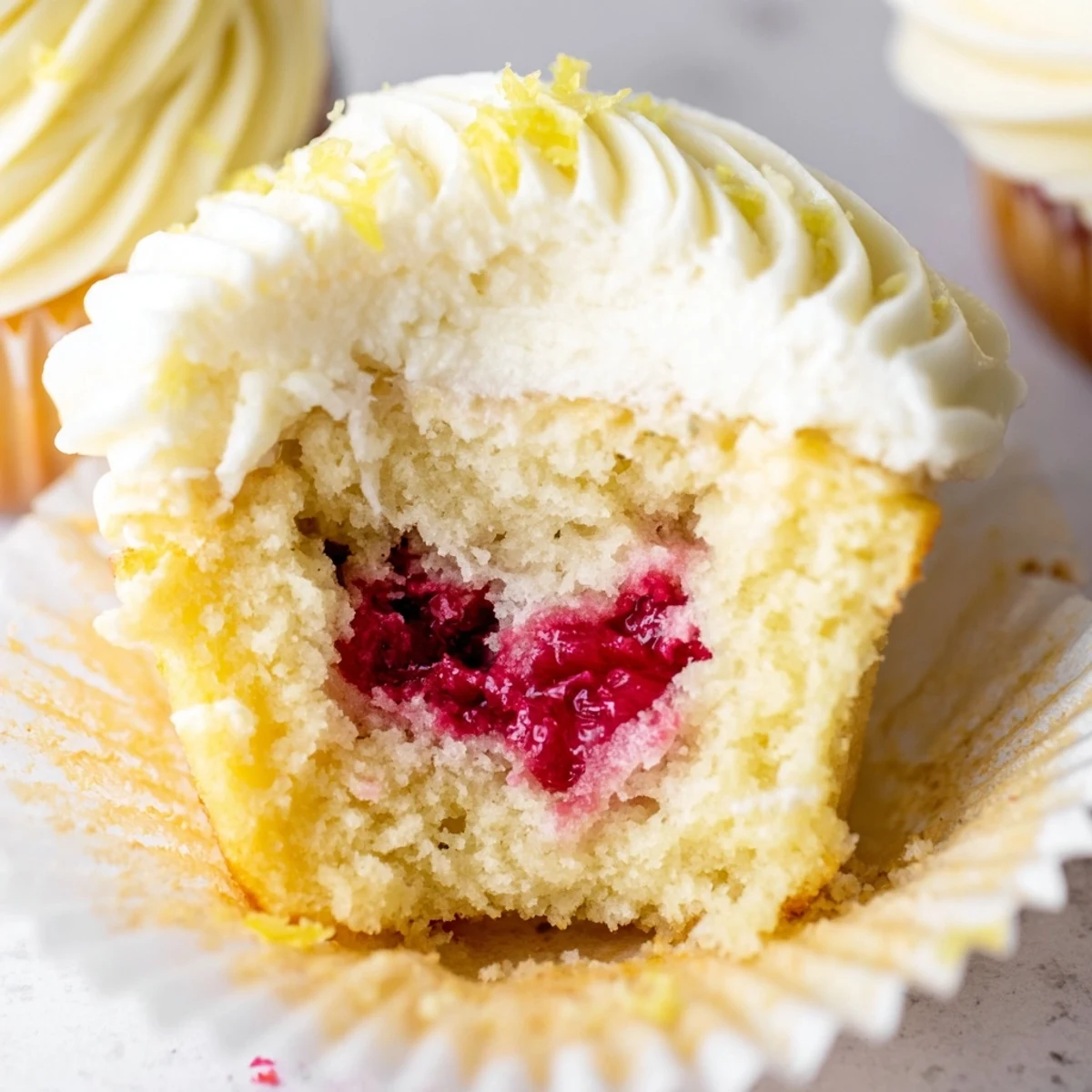 Tender lemon cupcakes featuring tart raspberry filling and smooth buttercream garnished with fresh lemon zest