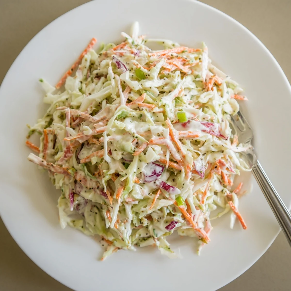 White bowl piled high with colorful easy creamy coleslaw topped with fresh green onion slices