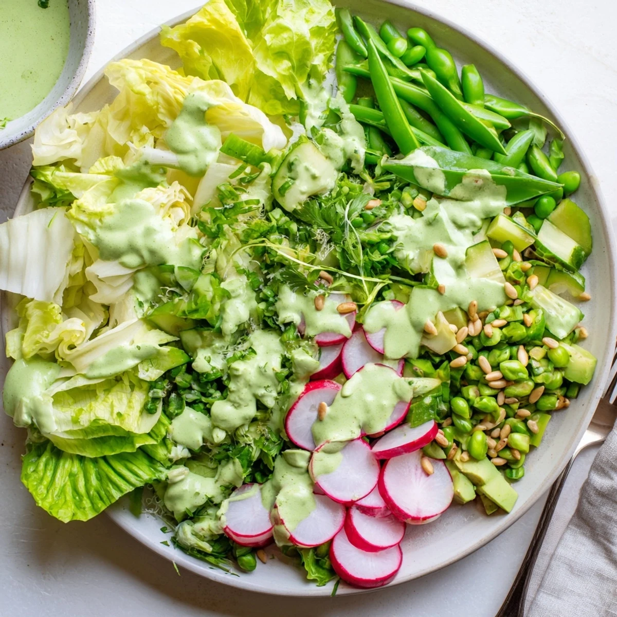 Vibrant green goddess salad featuring avocado, cucumber, and snap peas drizzled with tangy herb dressing