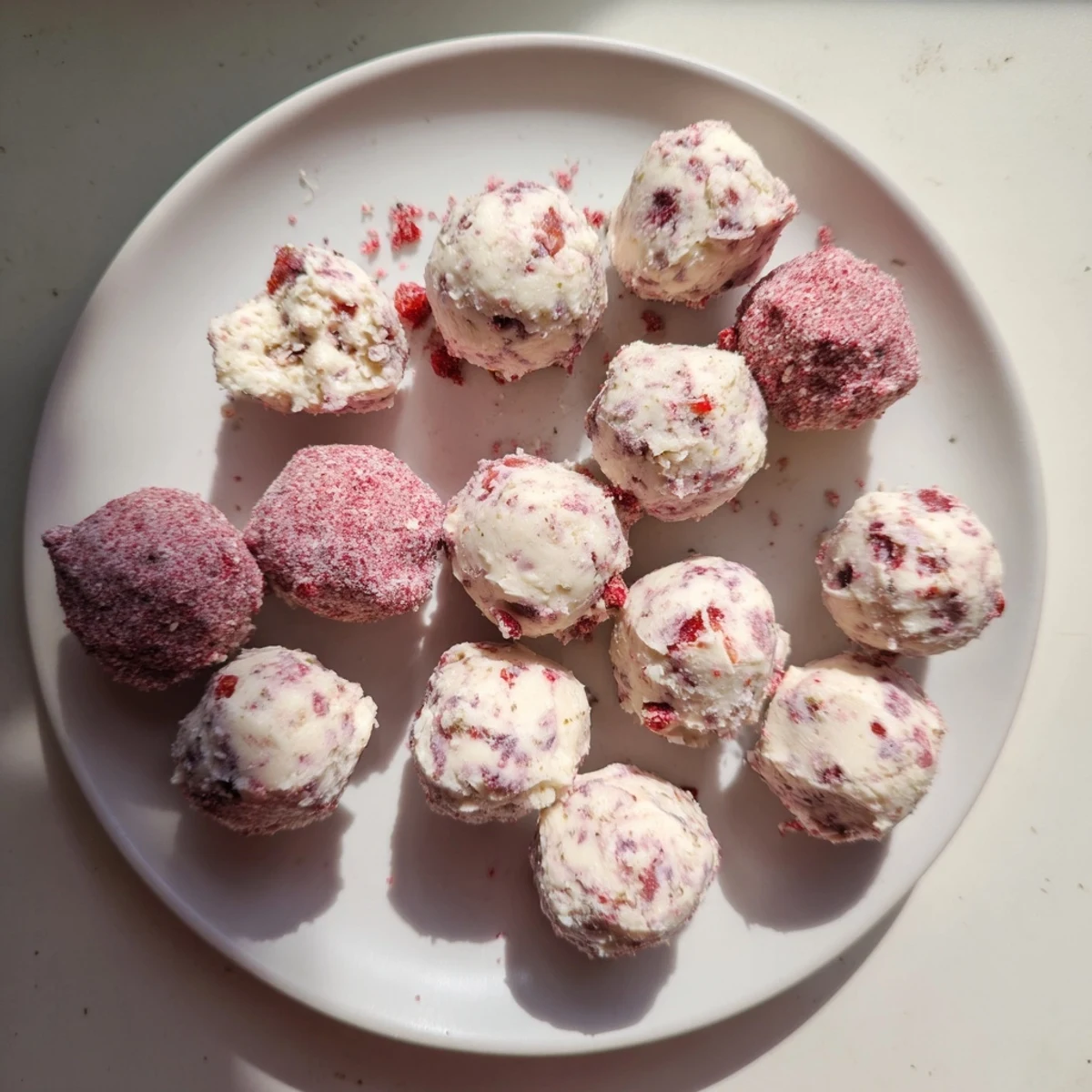 Bite-sized strawberry cheesecake fat bombs arranged on parchment paper with fresh strawberry pieces scattered around