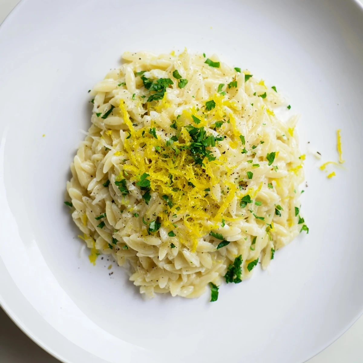 Creamy lemon orzo pasta with fresh herbs and parmesan in a white bowl