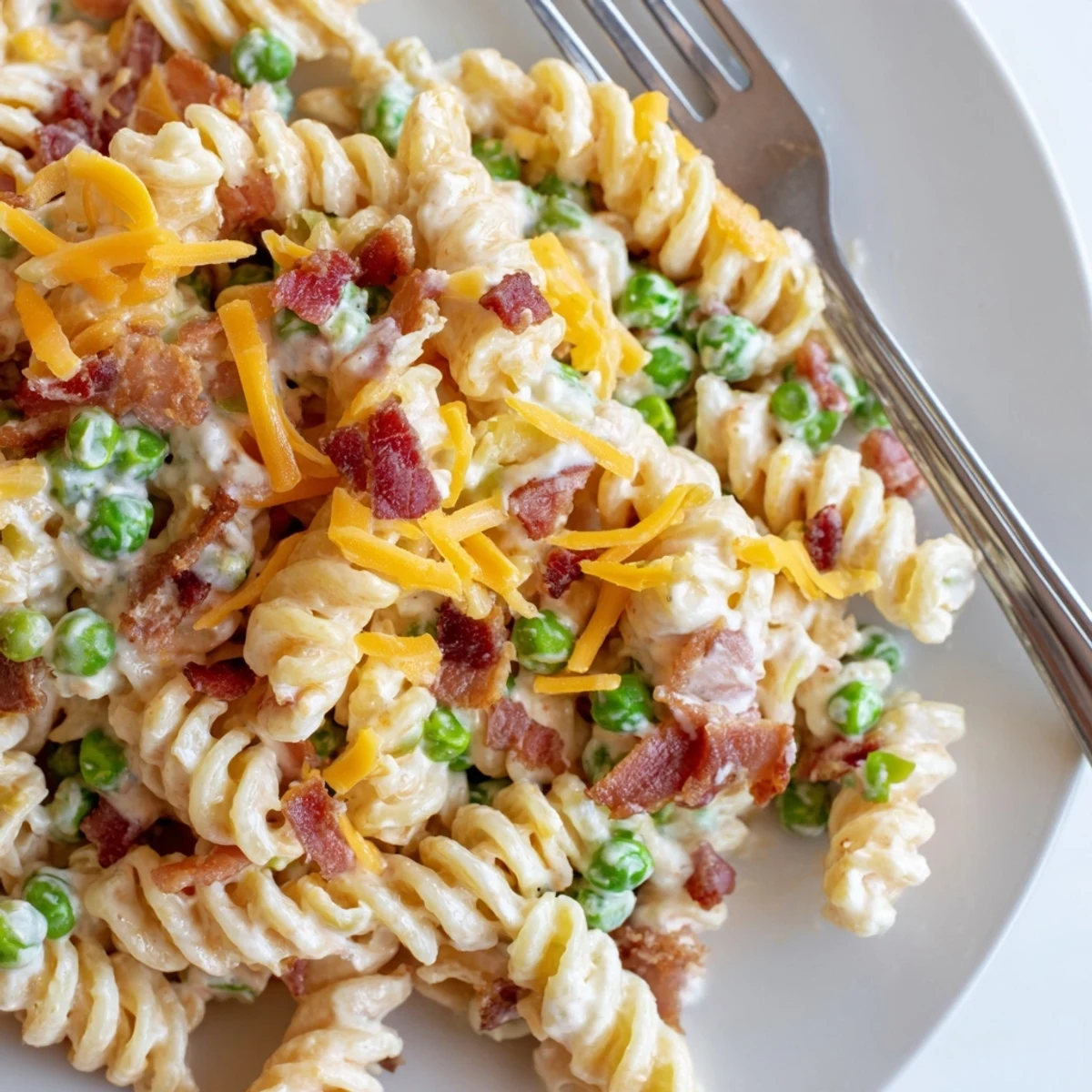 Hearty crack pasta salad featuring melted cheddar, savory bacon bits, and fresh peas ready for a summer picnic