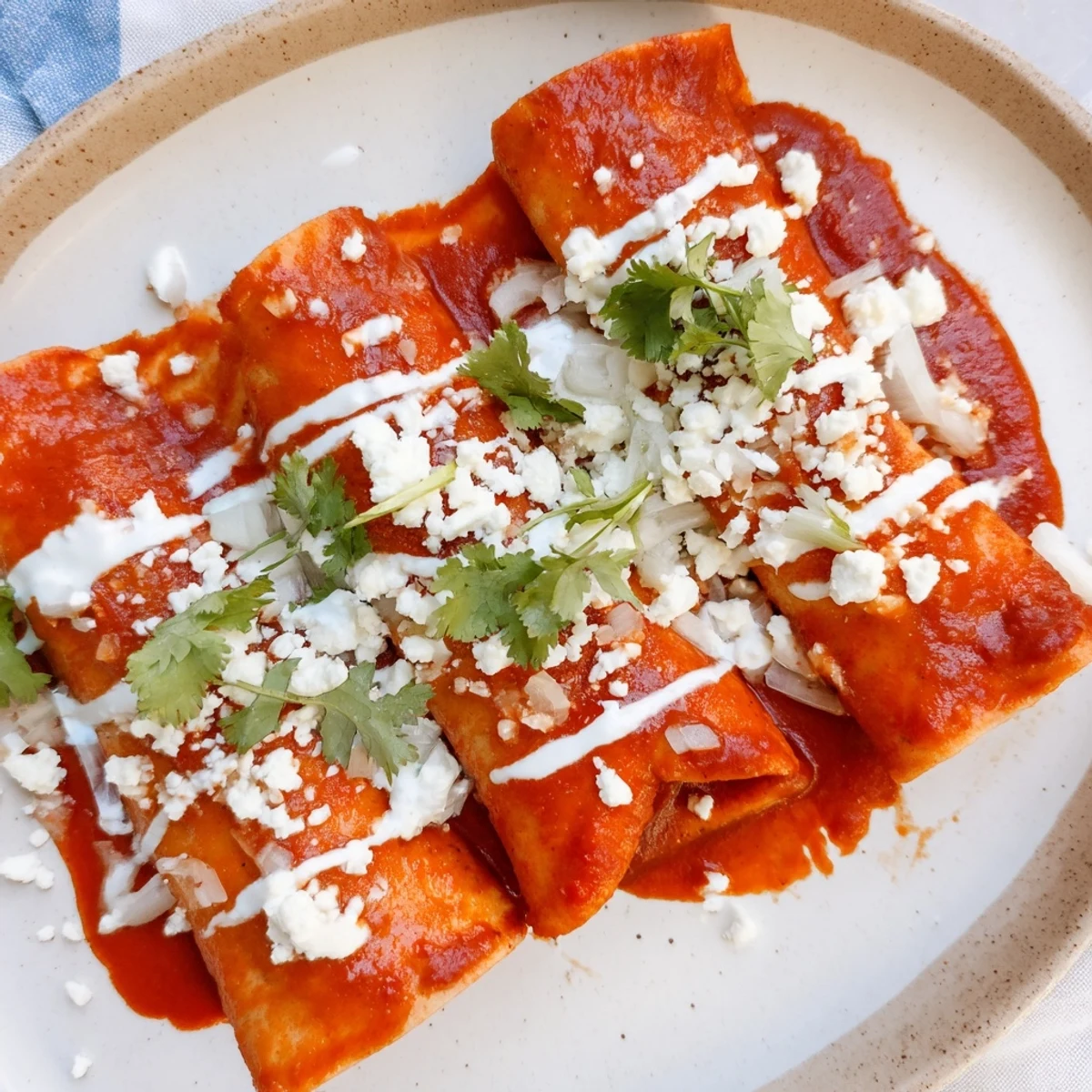 Entomatadas topped with crumbled cheese, fresh cilantro, and creamy drizzle on rustic plate