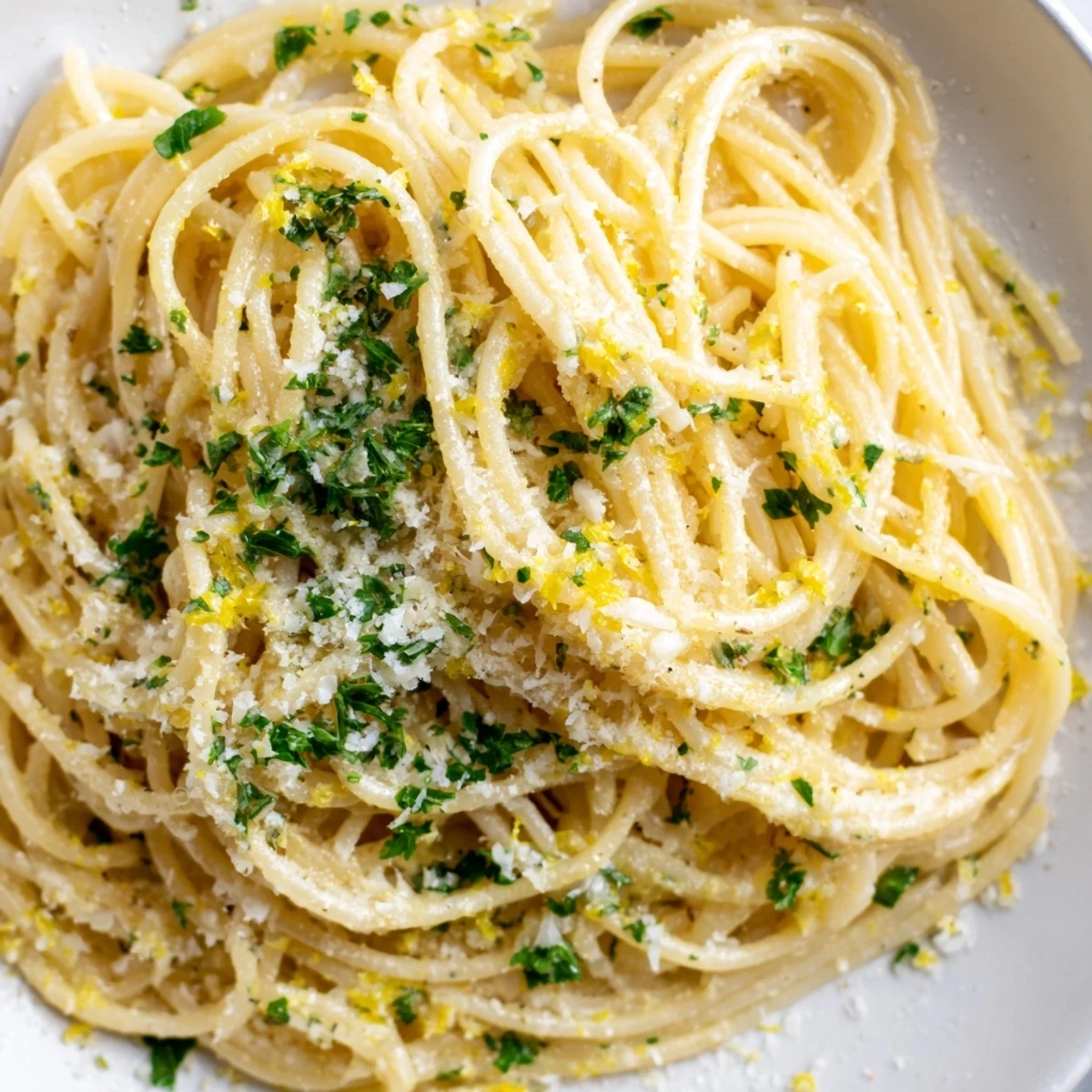 Creamy Parmesan lemon pasta tangled in strands with golden butter sauce and fresh herbs