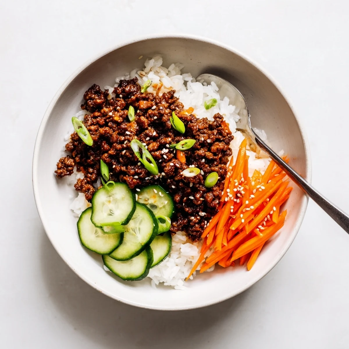 Savory Korean beef bowls topped with fresh cucumber, carrots, and sesame seeds over steamed white rice