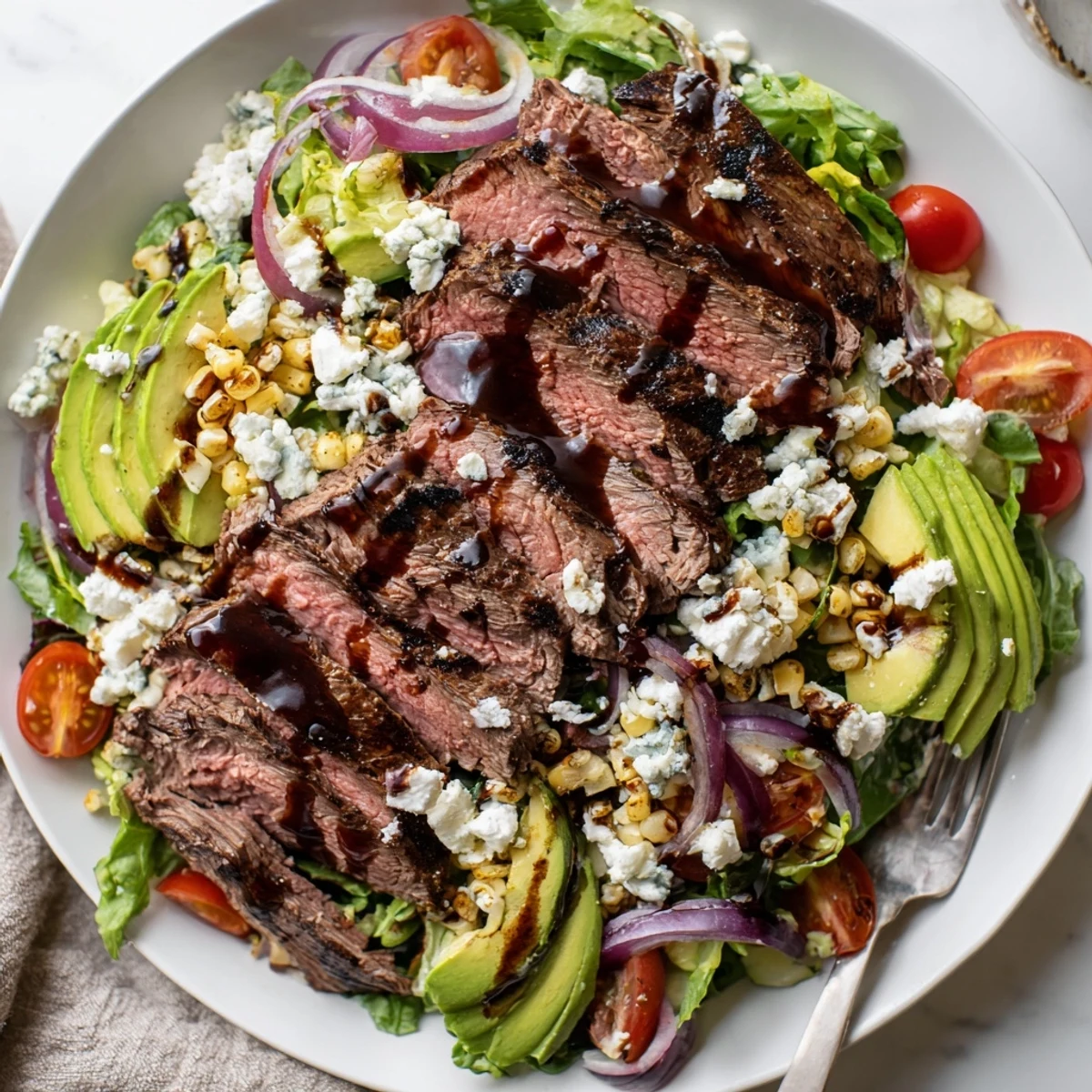 A generous platter of balsamic steak Gorgonzola salad drizzled with vinaigrette beside juicy cherry tomatoes and avocado.