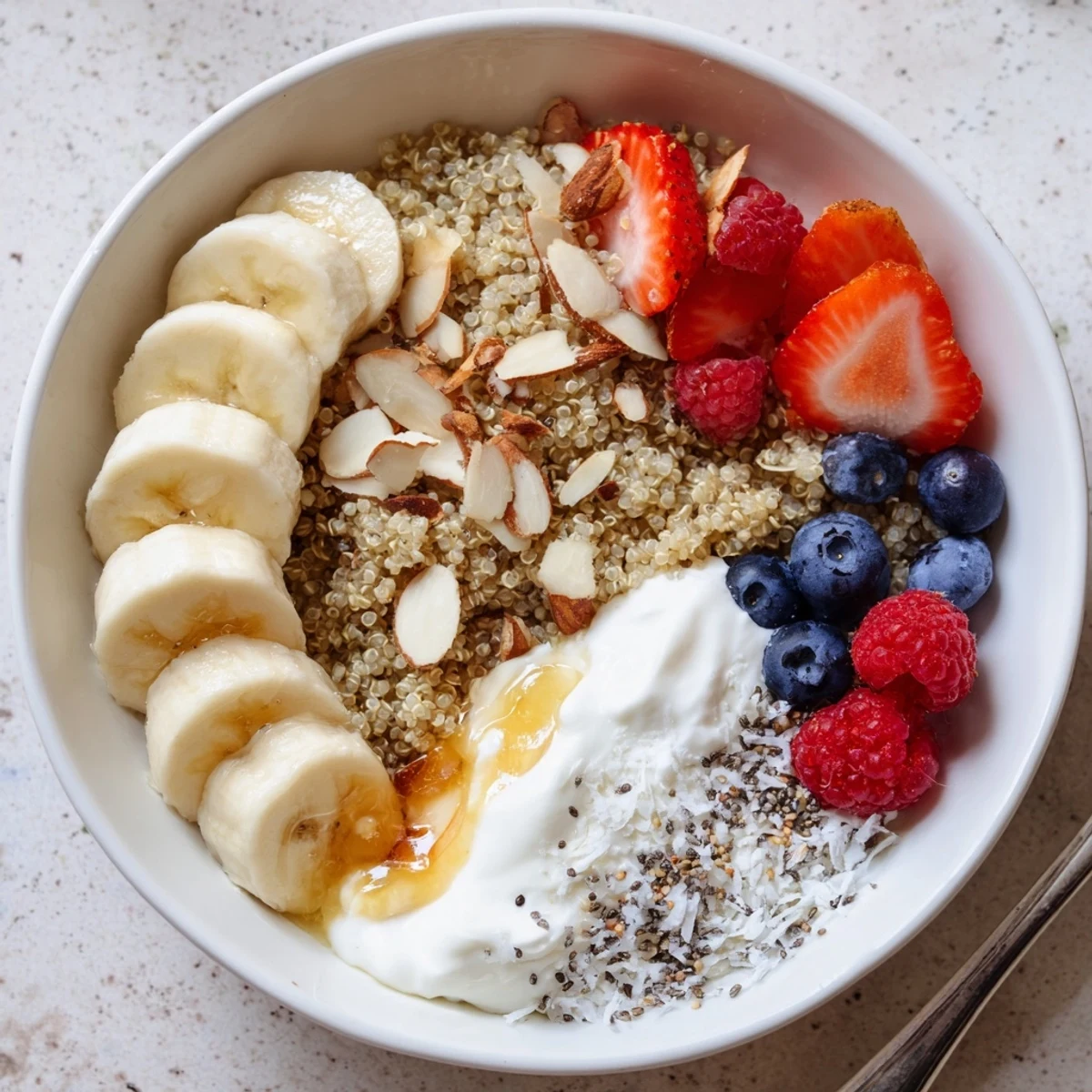 Fresh Quinoa Breakfast Bowl topped with sliced banana, berries, crunchy nuts