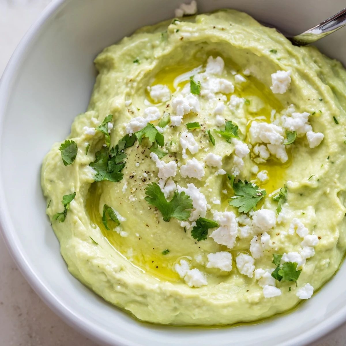 Creamy Avocado Feta Dip in a bowl, drizzled olive oil, chopped cilantro